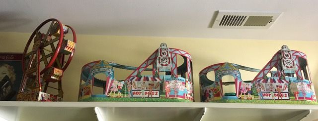 Colorful miniature carnival ride models displayed on a shelf under a ceiling vent.