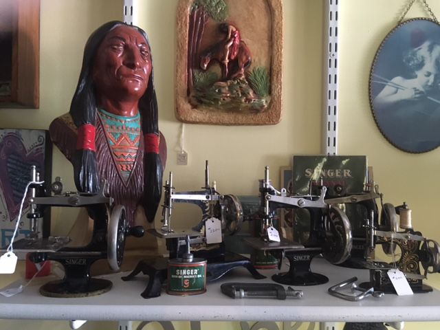Vintage sewing machine display with decorative figurines and framed wall art on a shelf