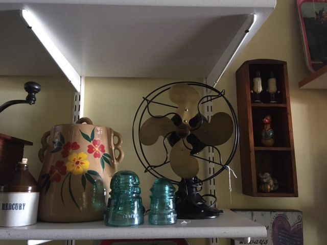Shelf with a floral jug, turquoise glass jars, and a black vintage fan in a kitchen nook