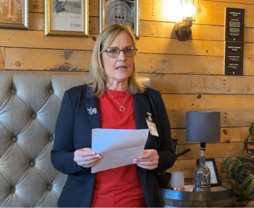 A woman stands smiling at the camera. She is reading a poem. 