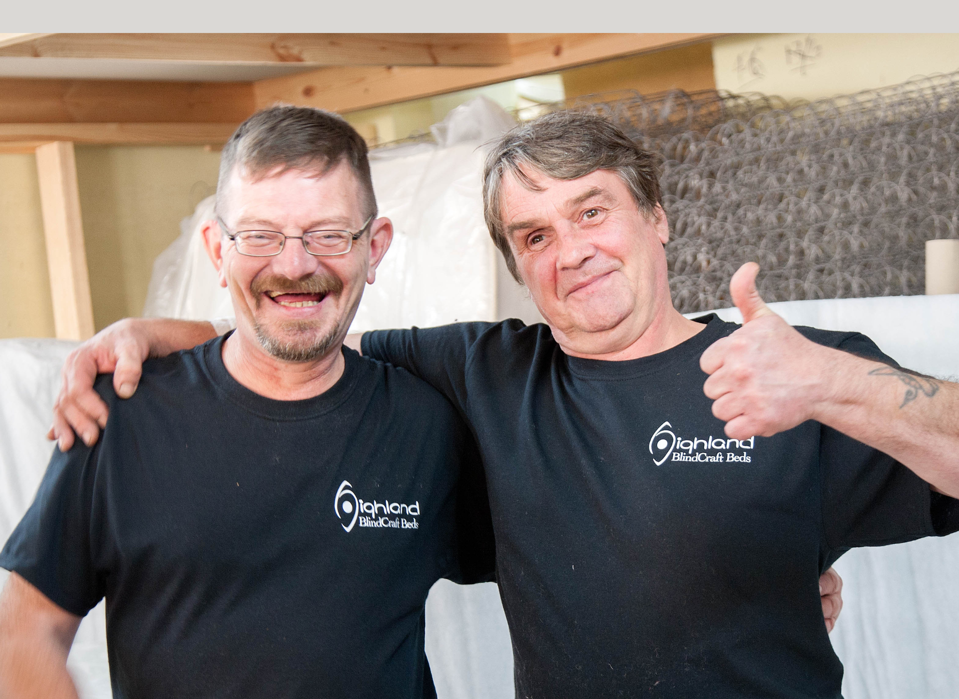 Two men smiling for the camera, wearing black tops. One man has his thumb up. 