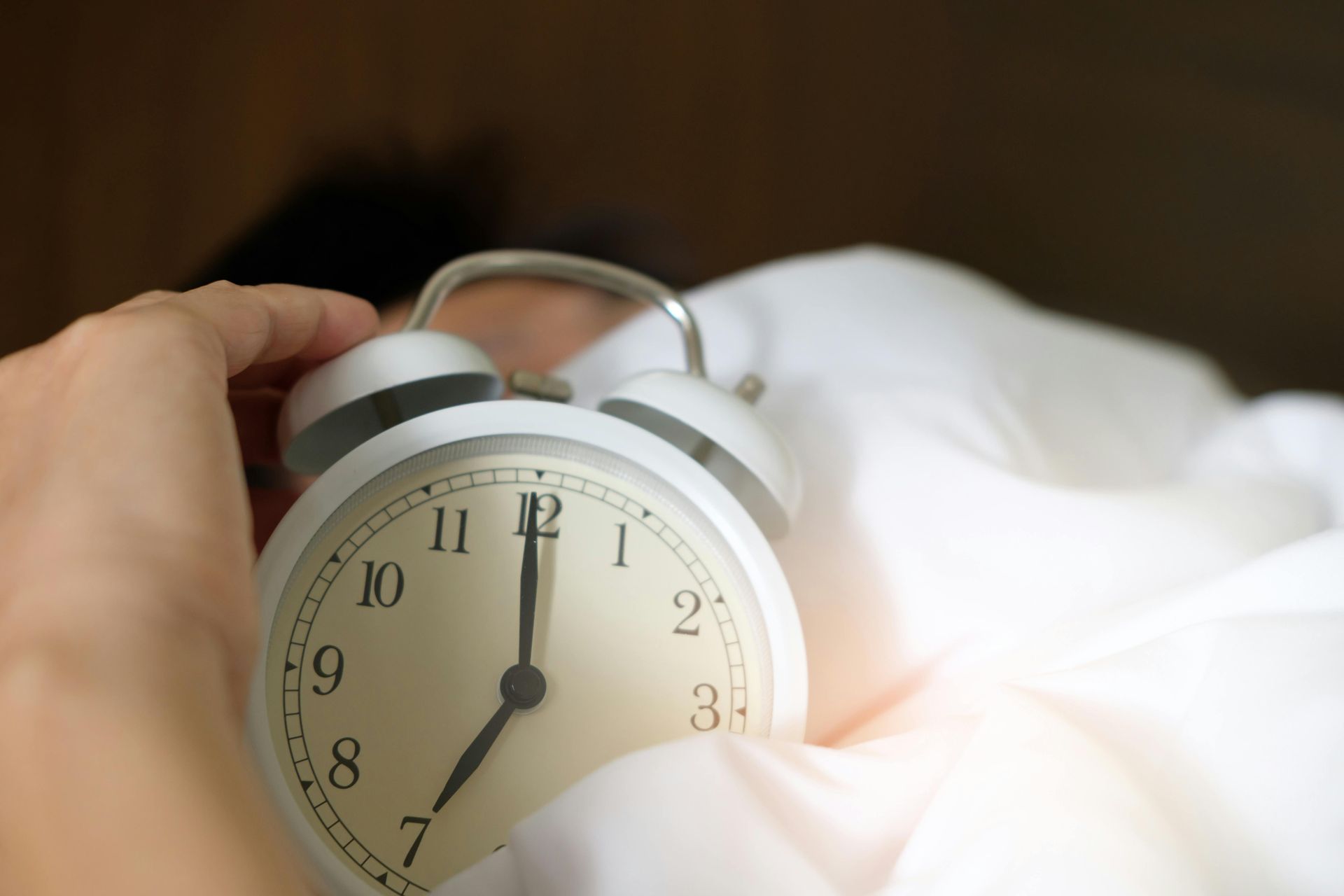 A person is holding an alarm clock in their hand while laying in bed.