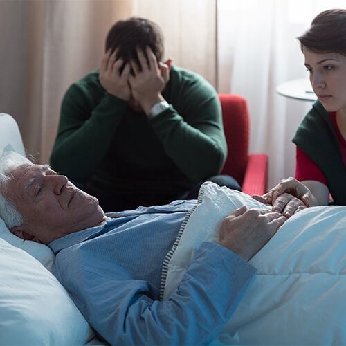 A man is laying in a hospital bed while a woman talks to him.