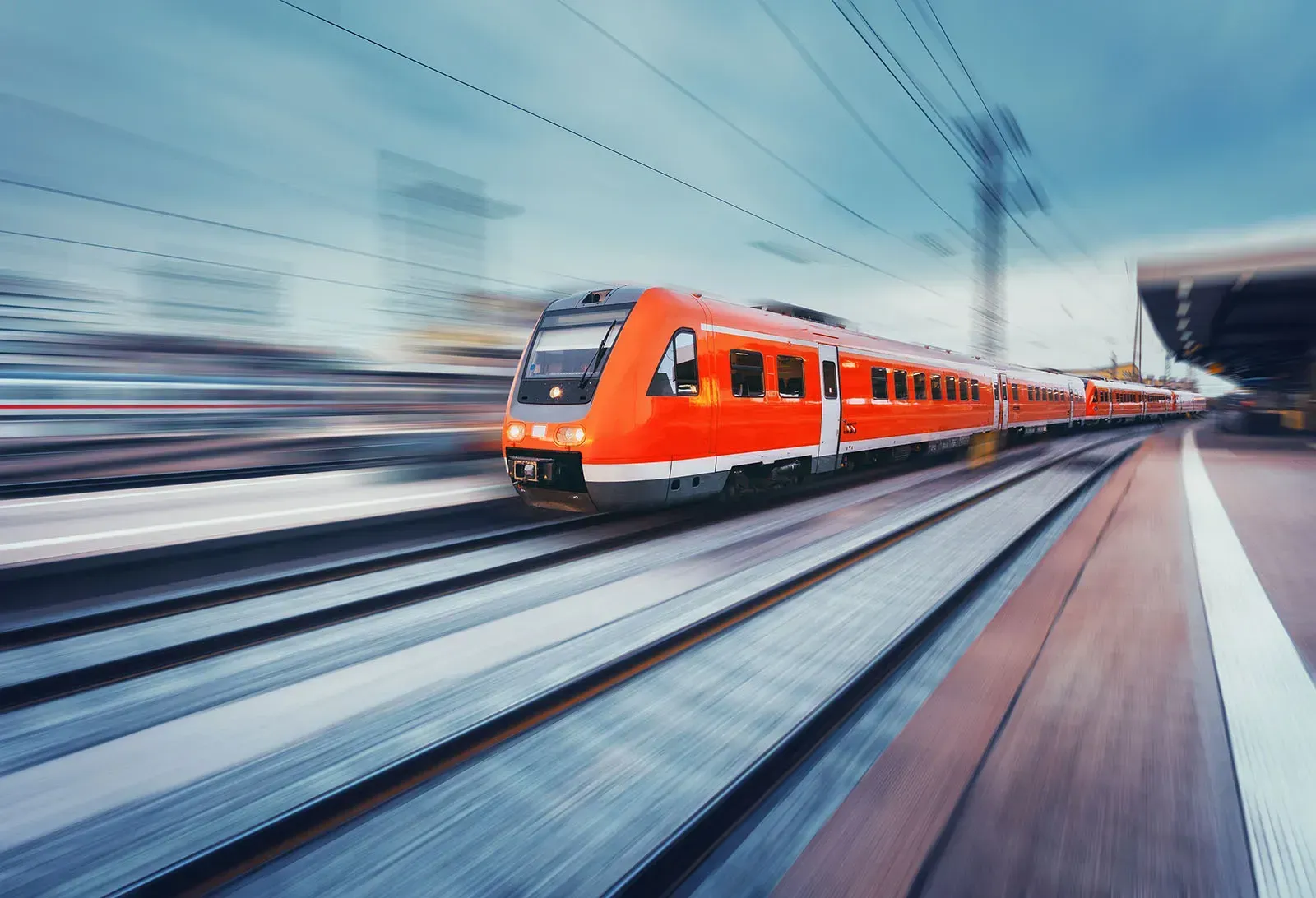 A red train is going down the tracks at a train station.