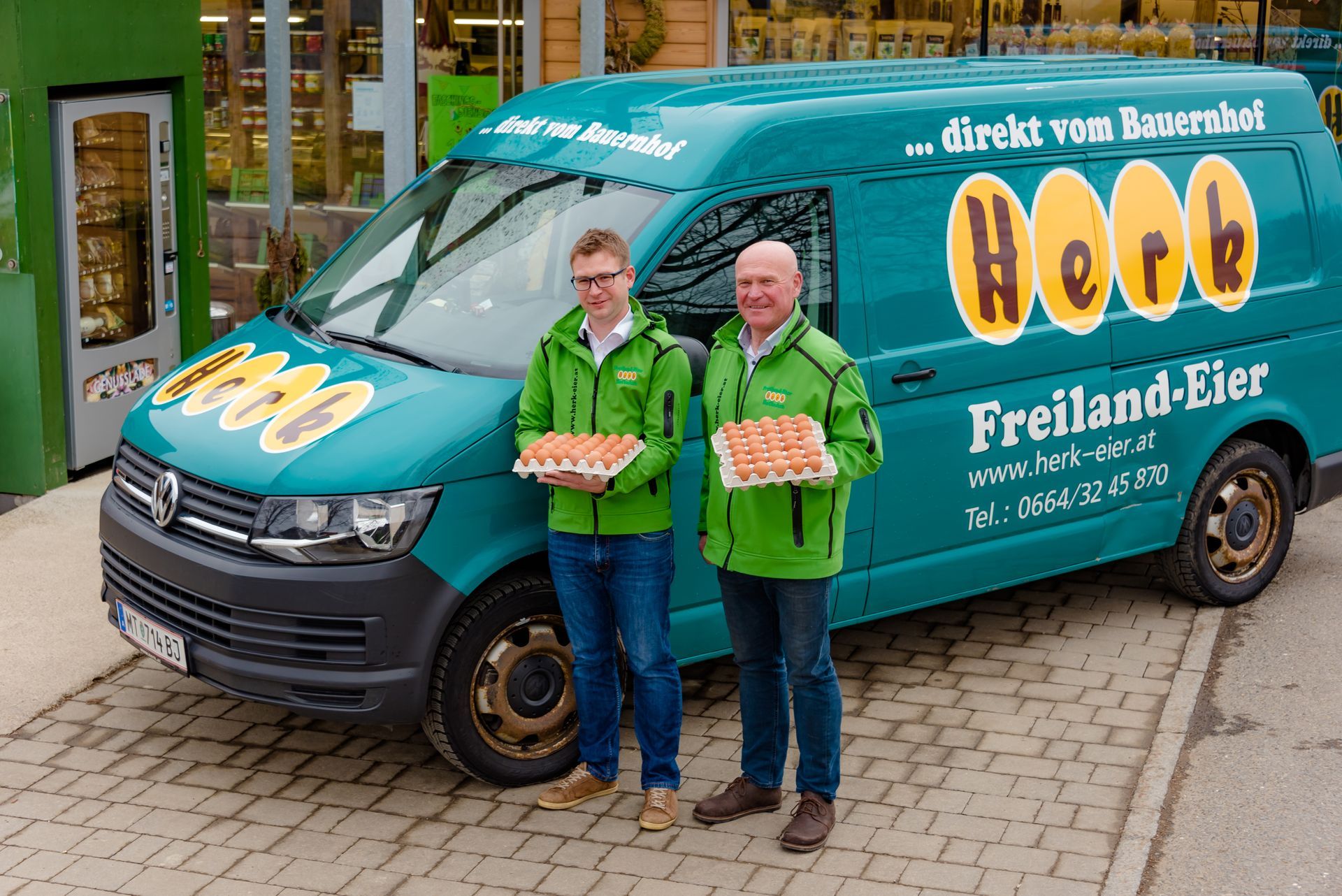 Zwei Personen in grünen Jacken stehen neben einem türkisfarbenen Lieferwagen der Brauerei Hooe.