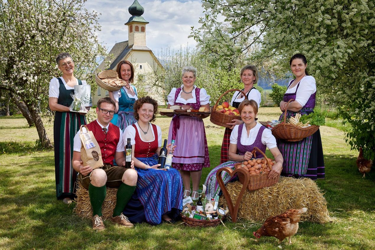Teamfoto Hofladen Herk im Garten mit Produkten und Freiland-Eiern und einem Huhn

