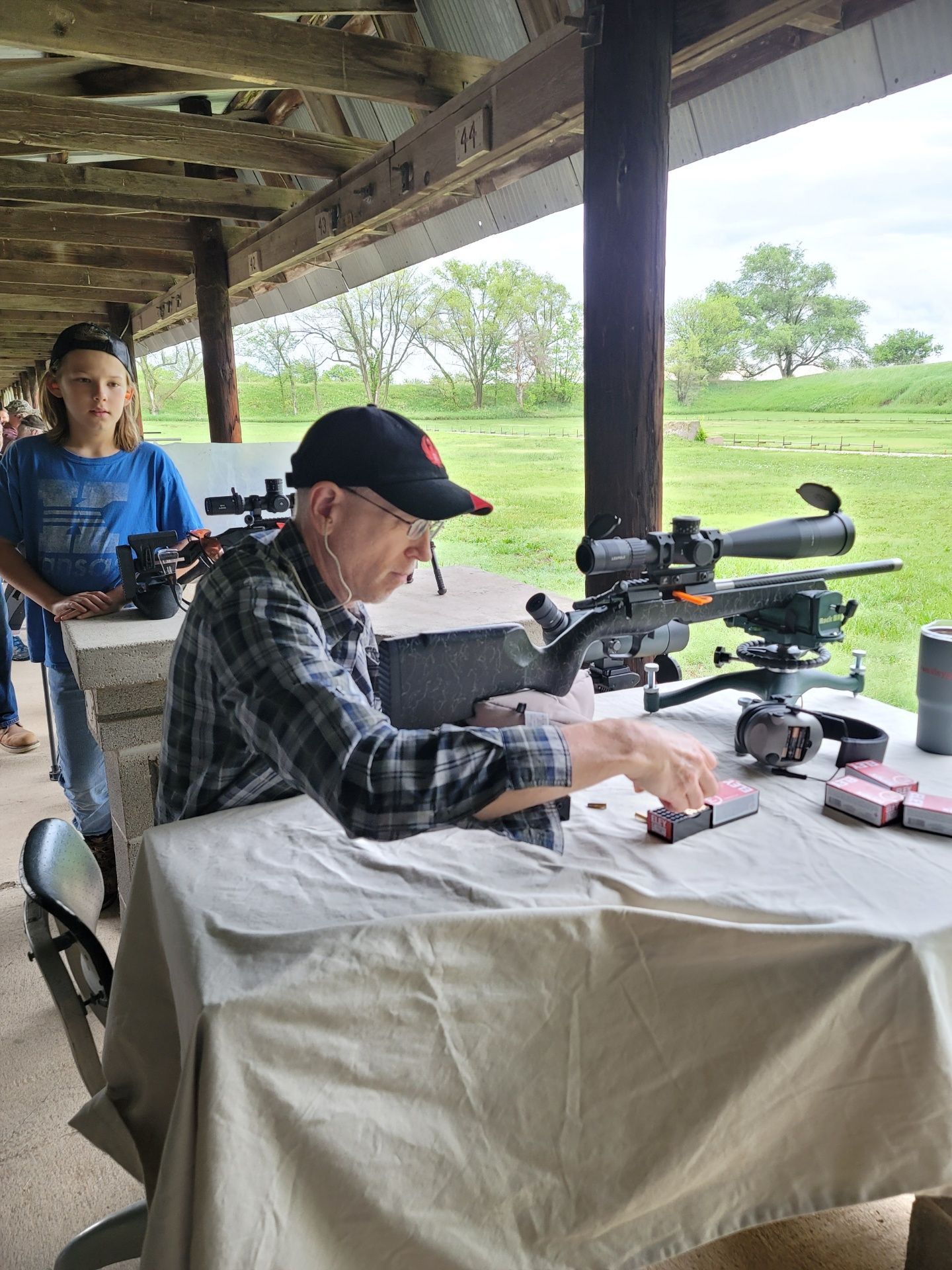 man in dark plaid shirt and black hat preparing to load ammo in rifle at gun range