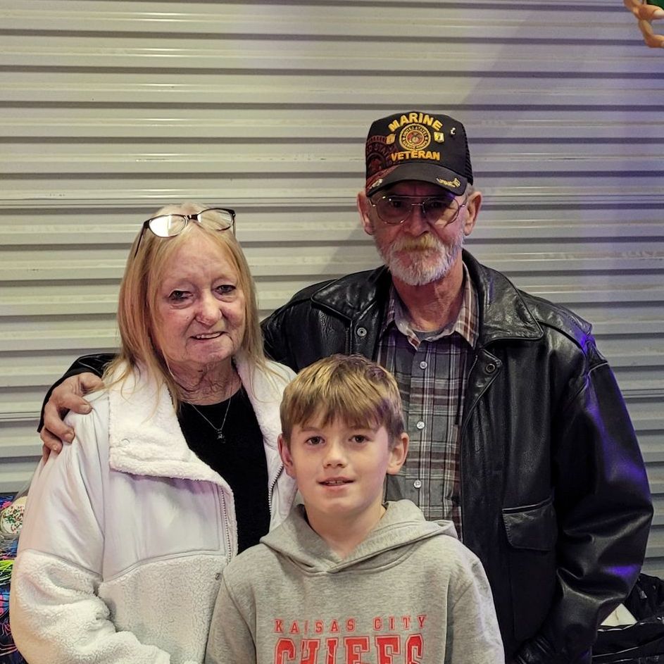 a boy wearing a kansas city chiefs sweatshirt poses with elderly couple