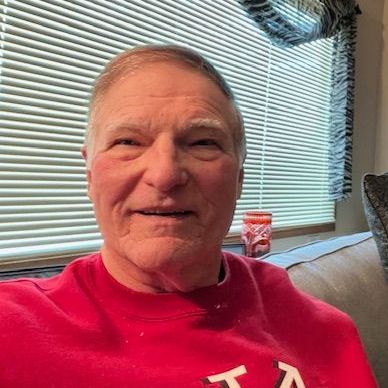 a man in a red sweater is sitting on a couch in front of a window .