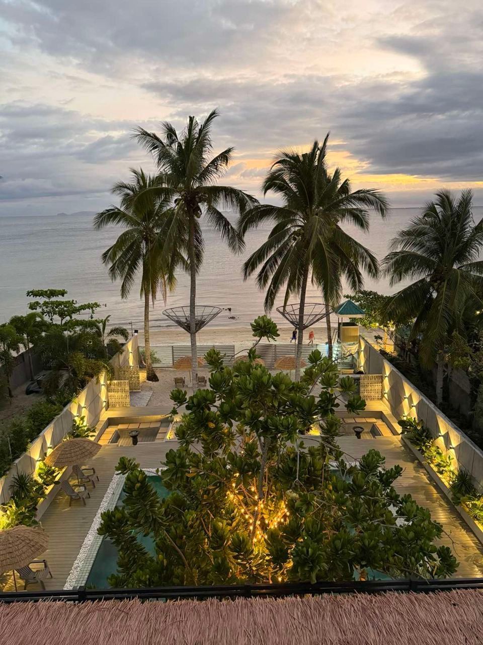An aerial view of a swimming pool surrounded by palm trees and a beach.