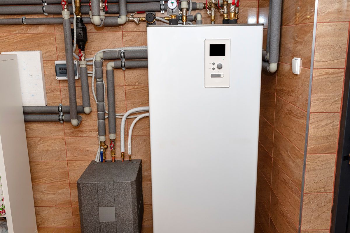 A white boiler is sitting in a room next to a brick wall.