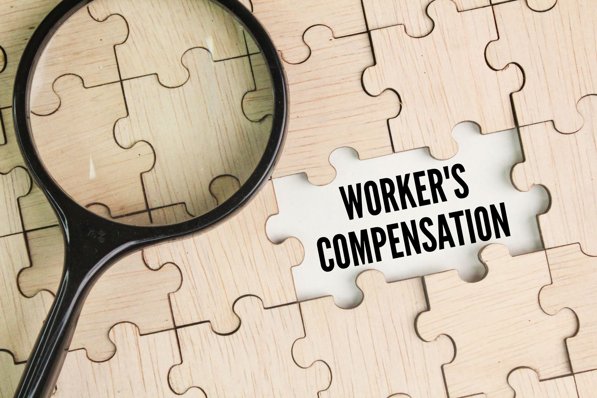 Magnifying glass and wooden puzzle with the word workers' compensation.