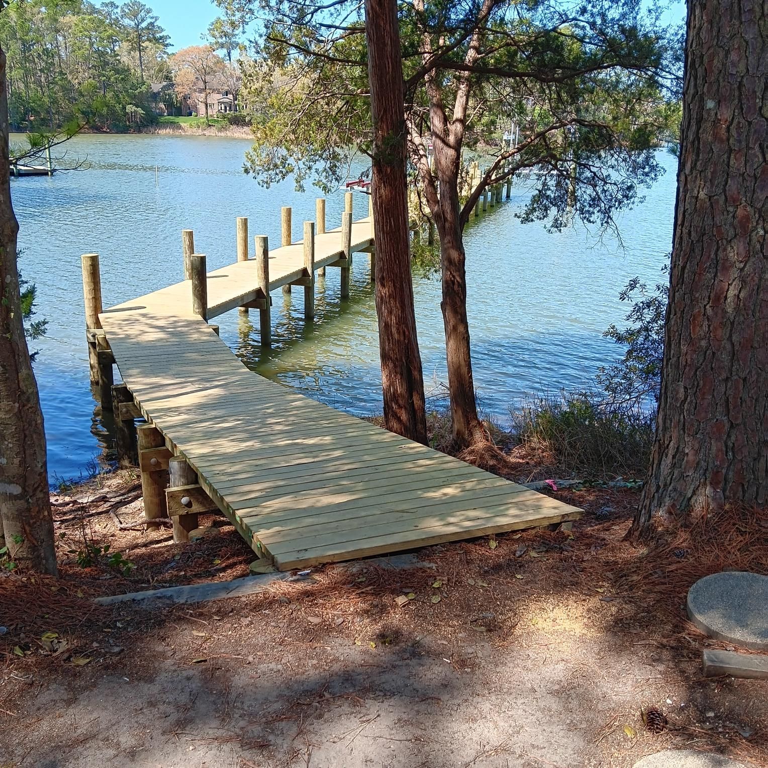 Wooden dock extending into a blue lake, seen between trees on a sunny day.