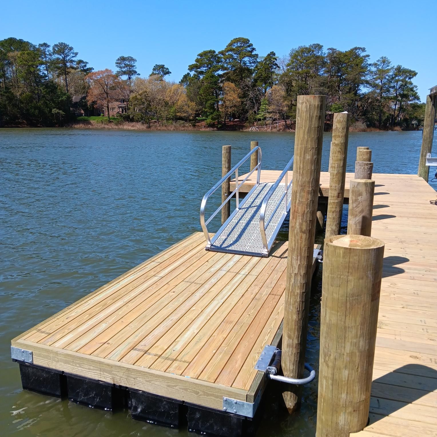 Wooden dock with ramp leading to deeper water. Water and trees in the background.