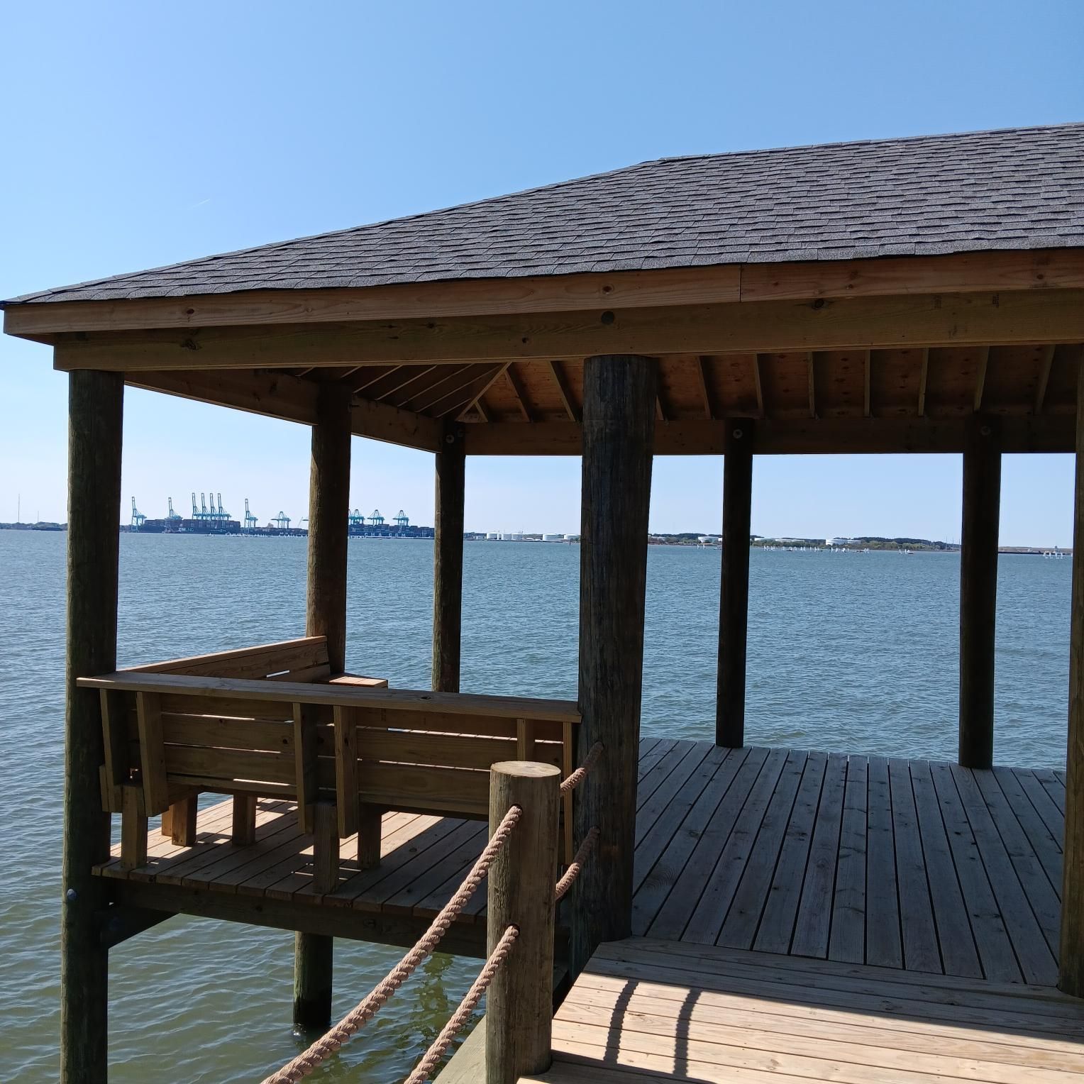 Wooden gazebo over water, with a bench, looking out at the ocean on a sunny day.
