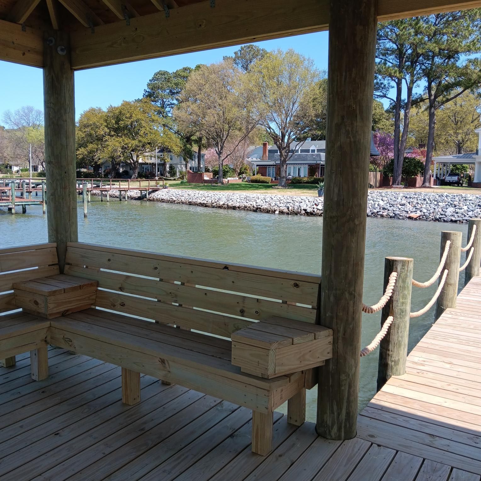 Dock with kayaks, water, and marsh under a blue sky.