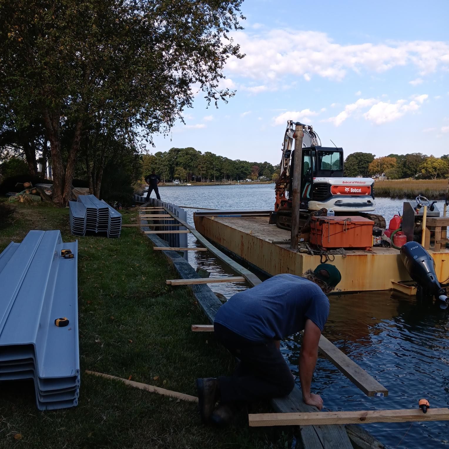 Construction workers installing shoreline materials near a body of water, with equipment and materials visible.