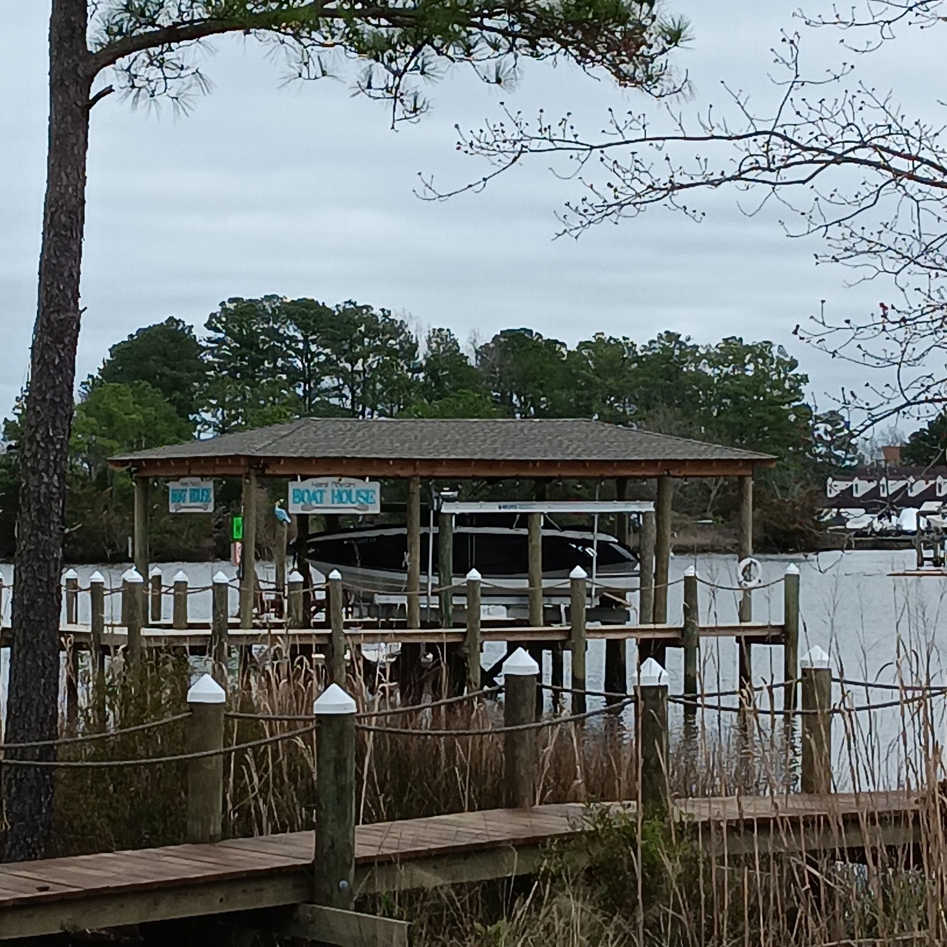 Pond edged with wooden beams, reflecting trees and a house with a deck. Gravel path alongside.