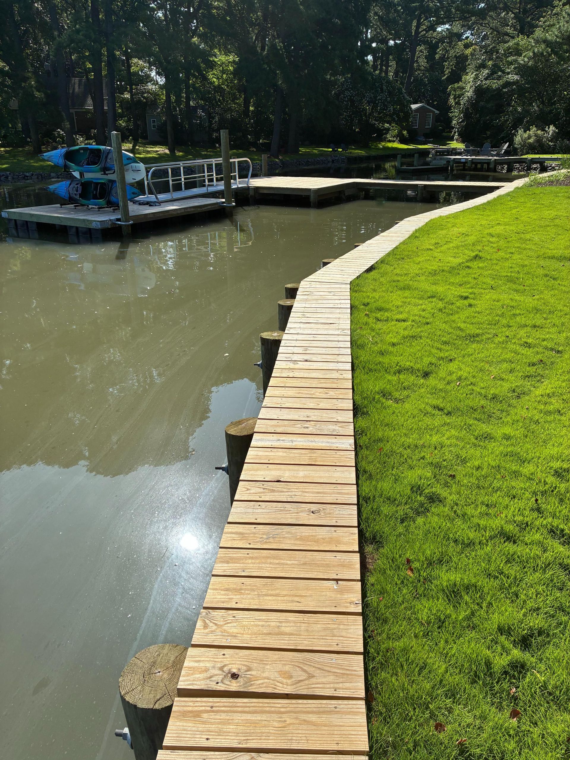 Wooden walkway along a waterway, leading to docks with boats. Green grass on the right.