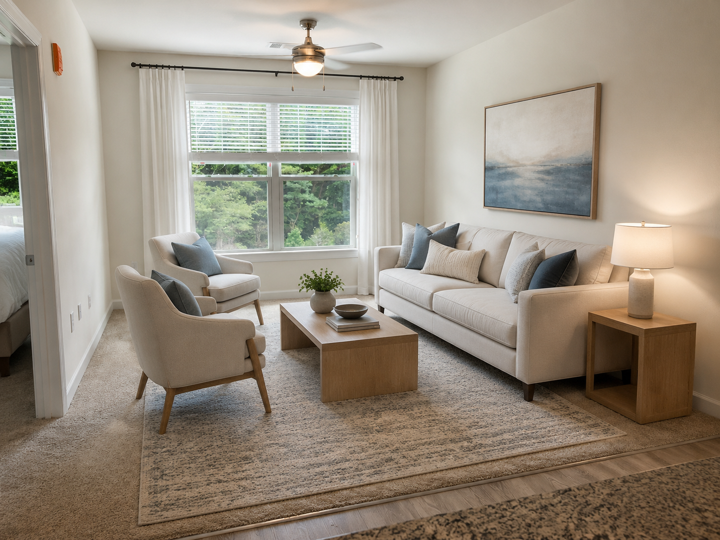 Bright living room with cream sofa, armchair, coffee table, rug, lamp, and large window with sheer curtains.