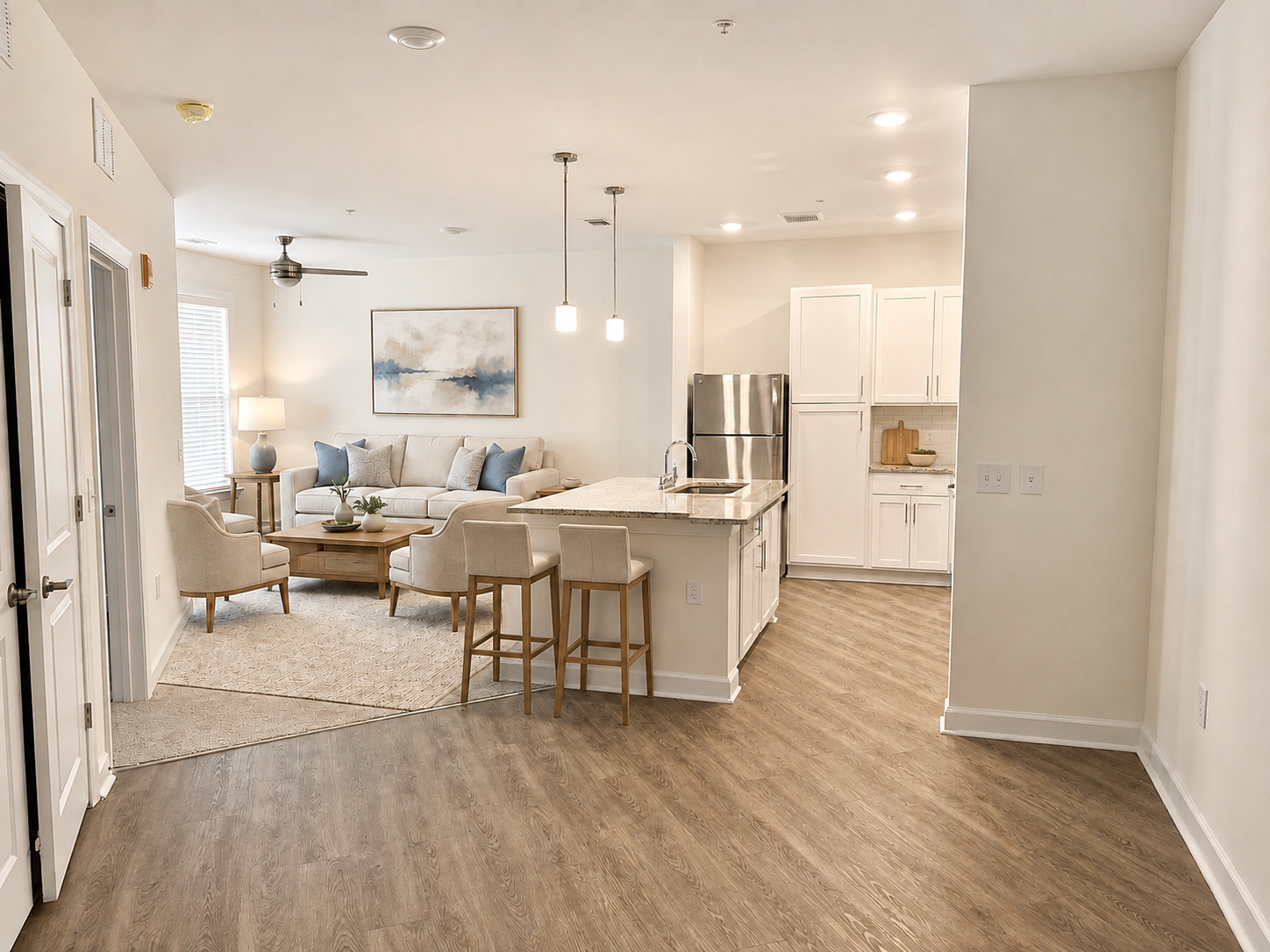 Bright open-concept living room and kitchen with white walls, wood floors, and beige furniture