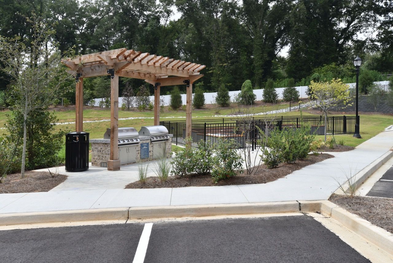 Parking lot with a pergola, picnic tables, landscaping, and a small pond or wetland area.