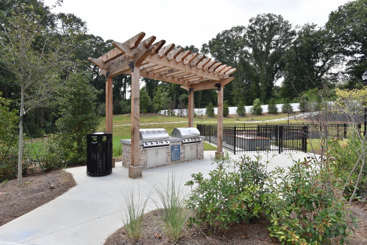 Outdoor communal grilling station under a wooden pergola with stainless grills.