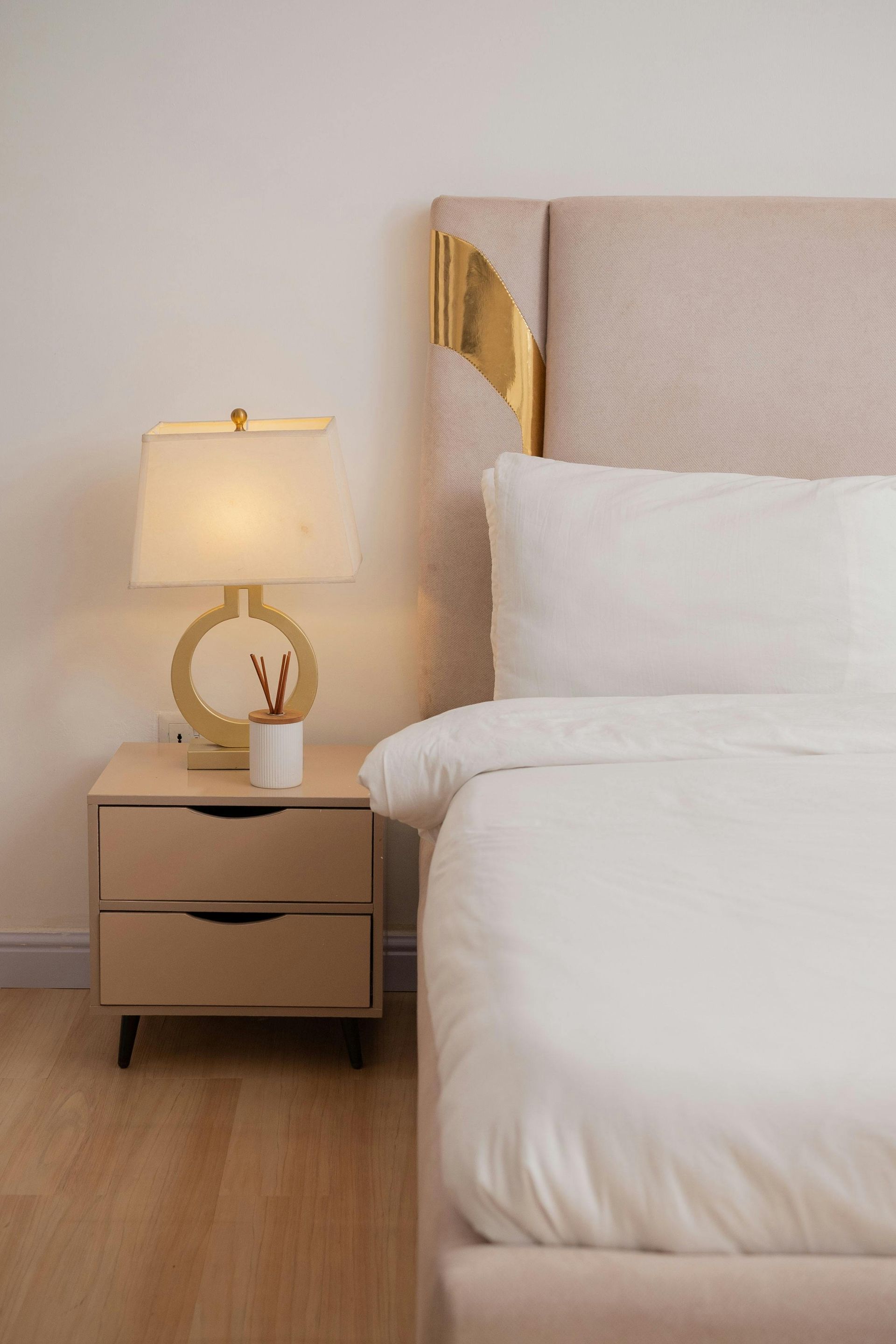 Modern bedroom with a neatly made white bed, bedside lamp, and wooden nightstand