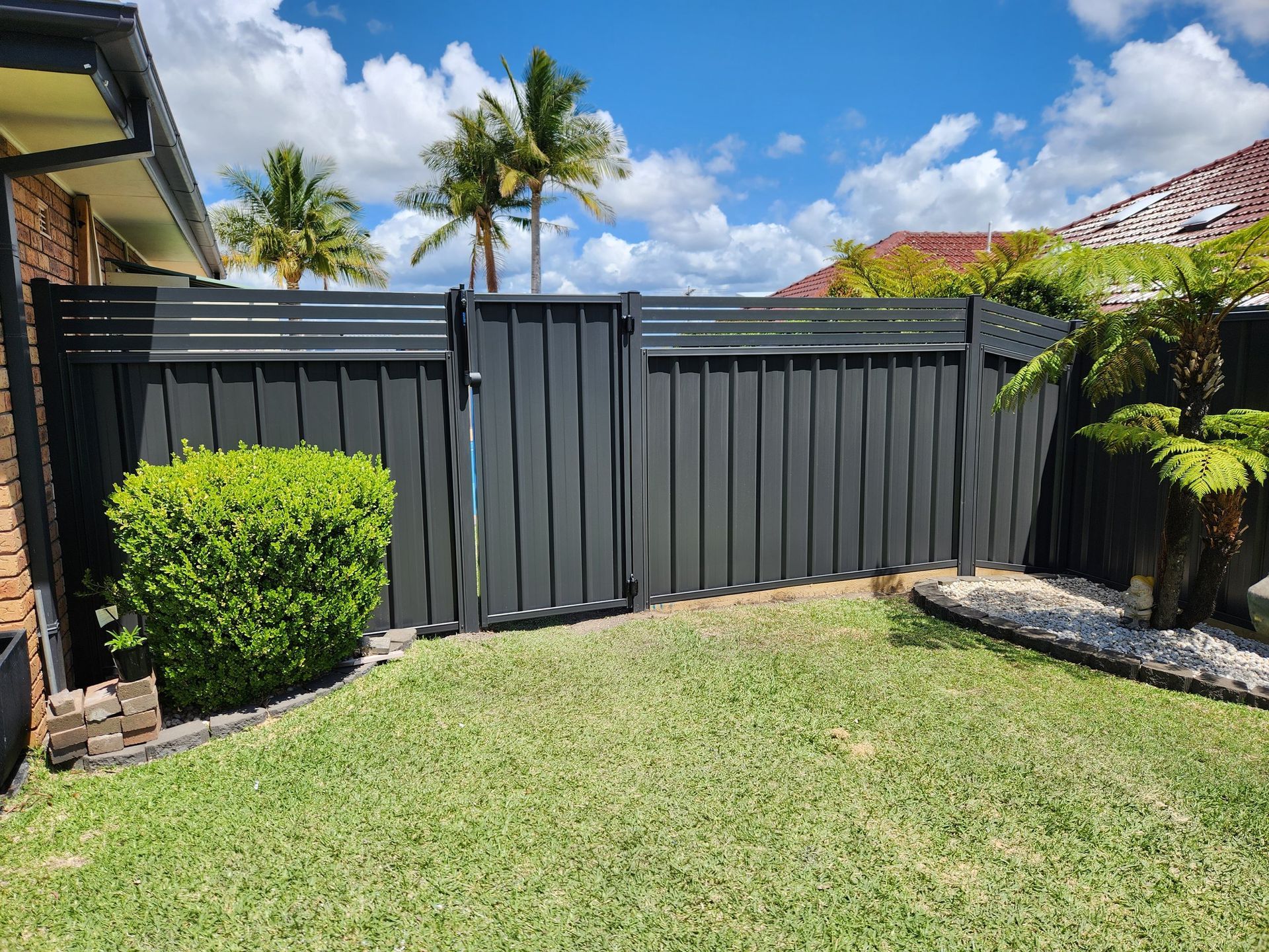 A black fence with a gate in the backyard of a house.