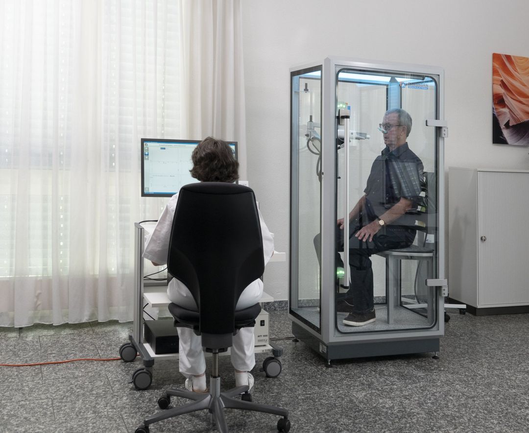 A man is sitting in a chair while a woman sits at a desk with a computer.