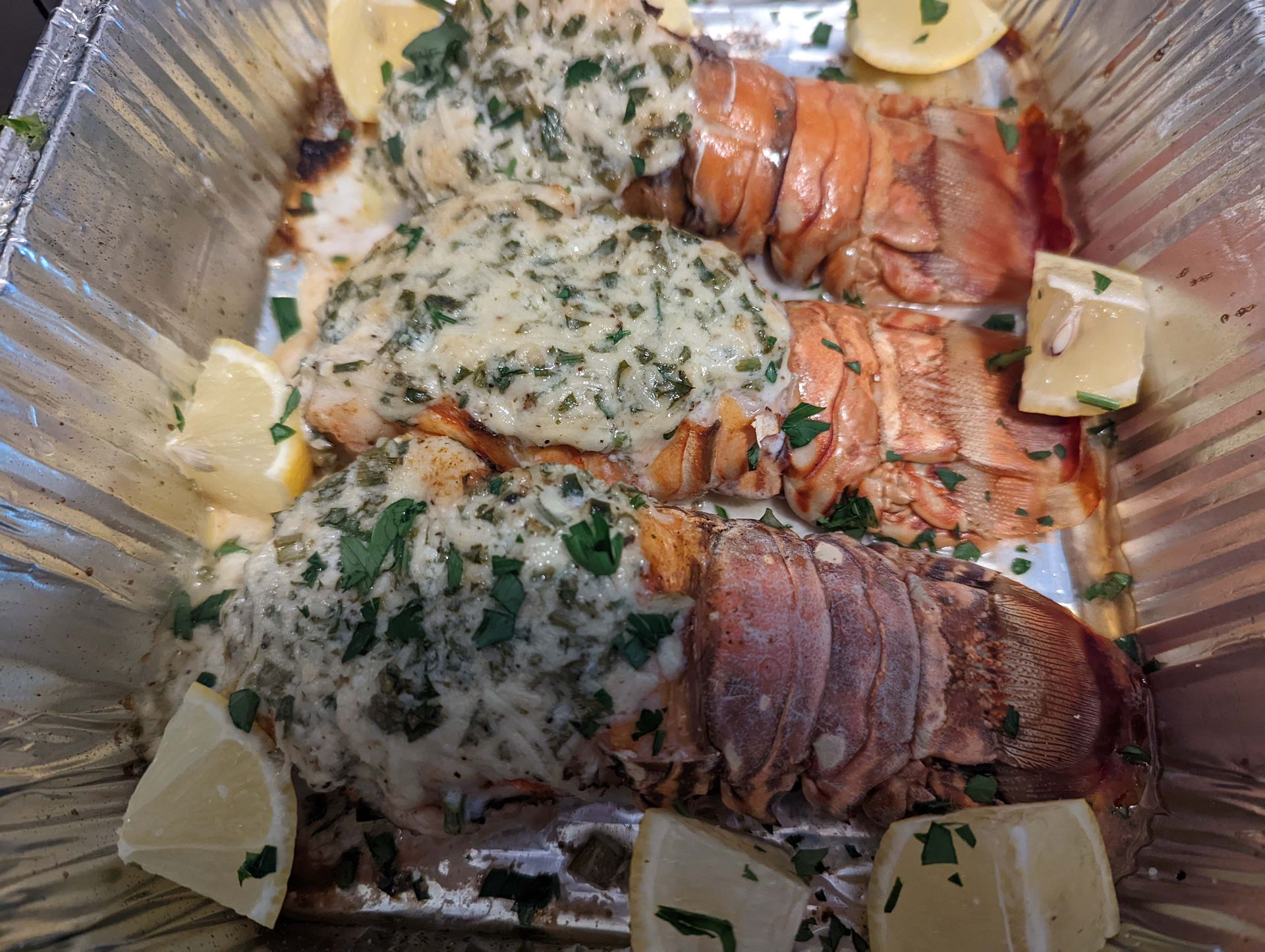 Aluminum foil container filled with a variety of food including lobster tails and chicken.