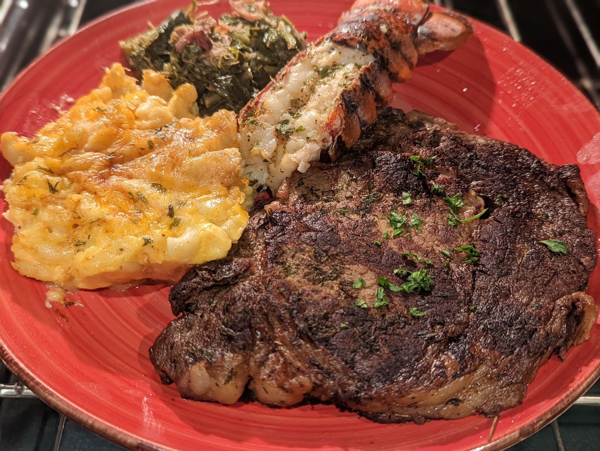 A red plate topped with a steak , macaroni and cheese , and spinach.