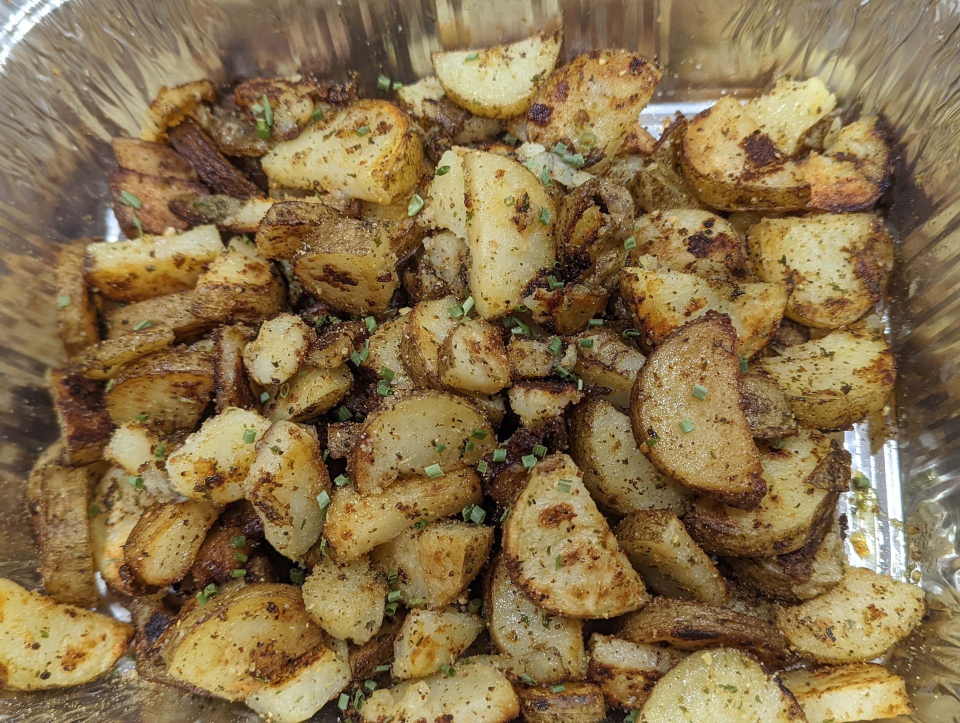 A foil container filled with fried potatoes and vegetables.
