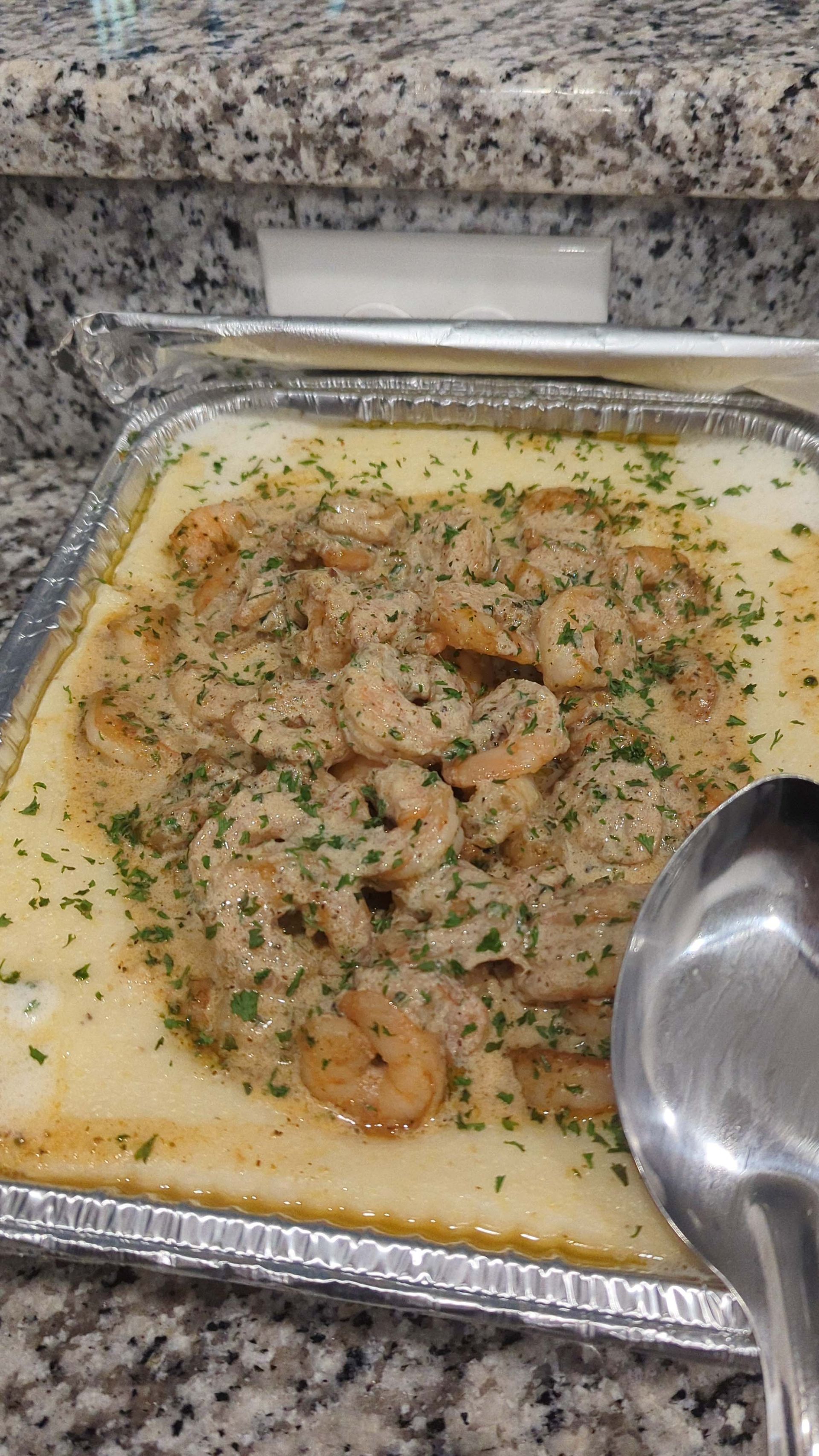 A casserole dish filled with shrimp and a spoon on a counter.