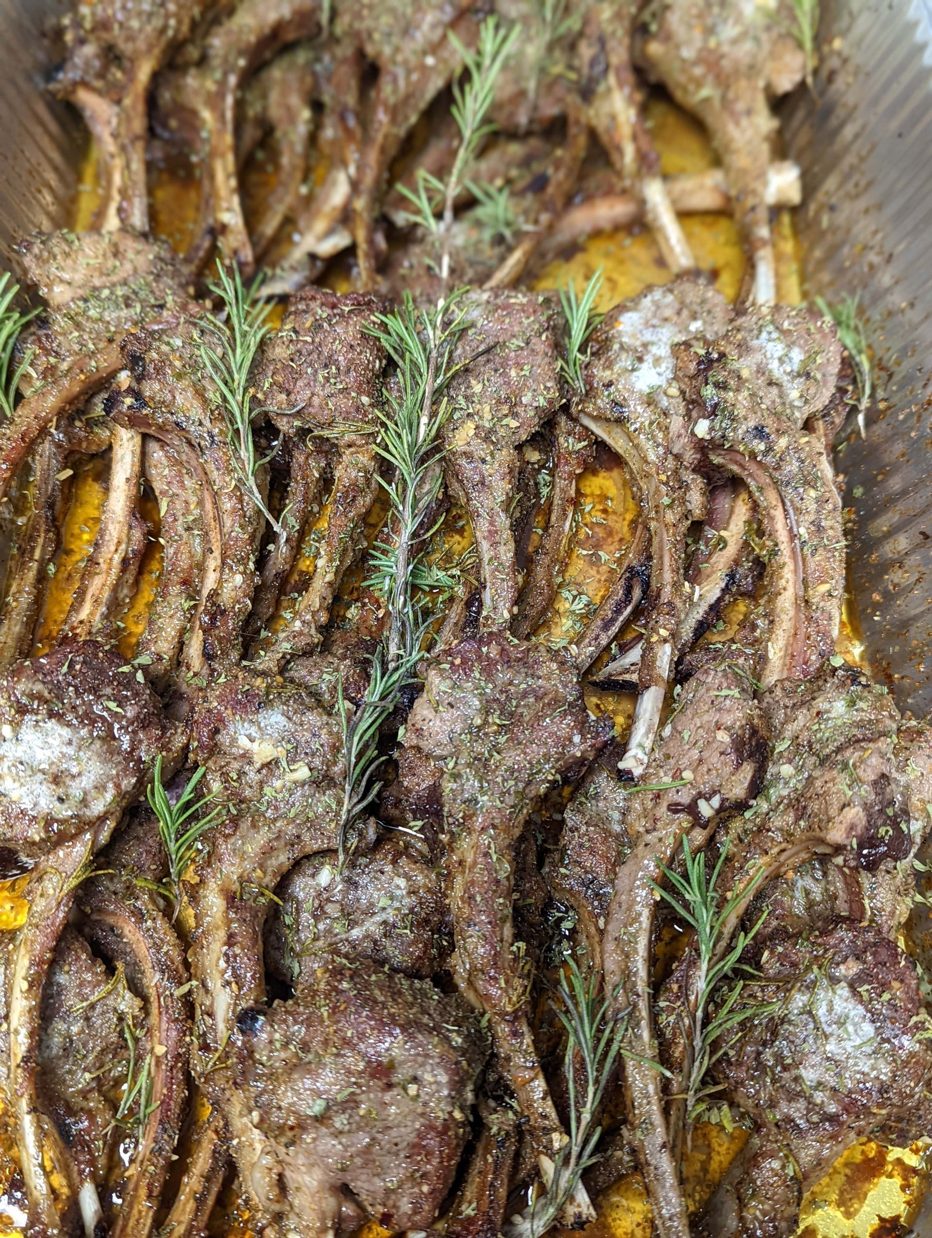 A close up of a tray of lamb chops with rosemary.