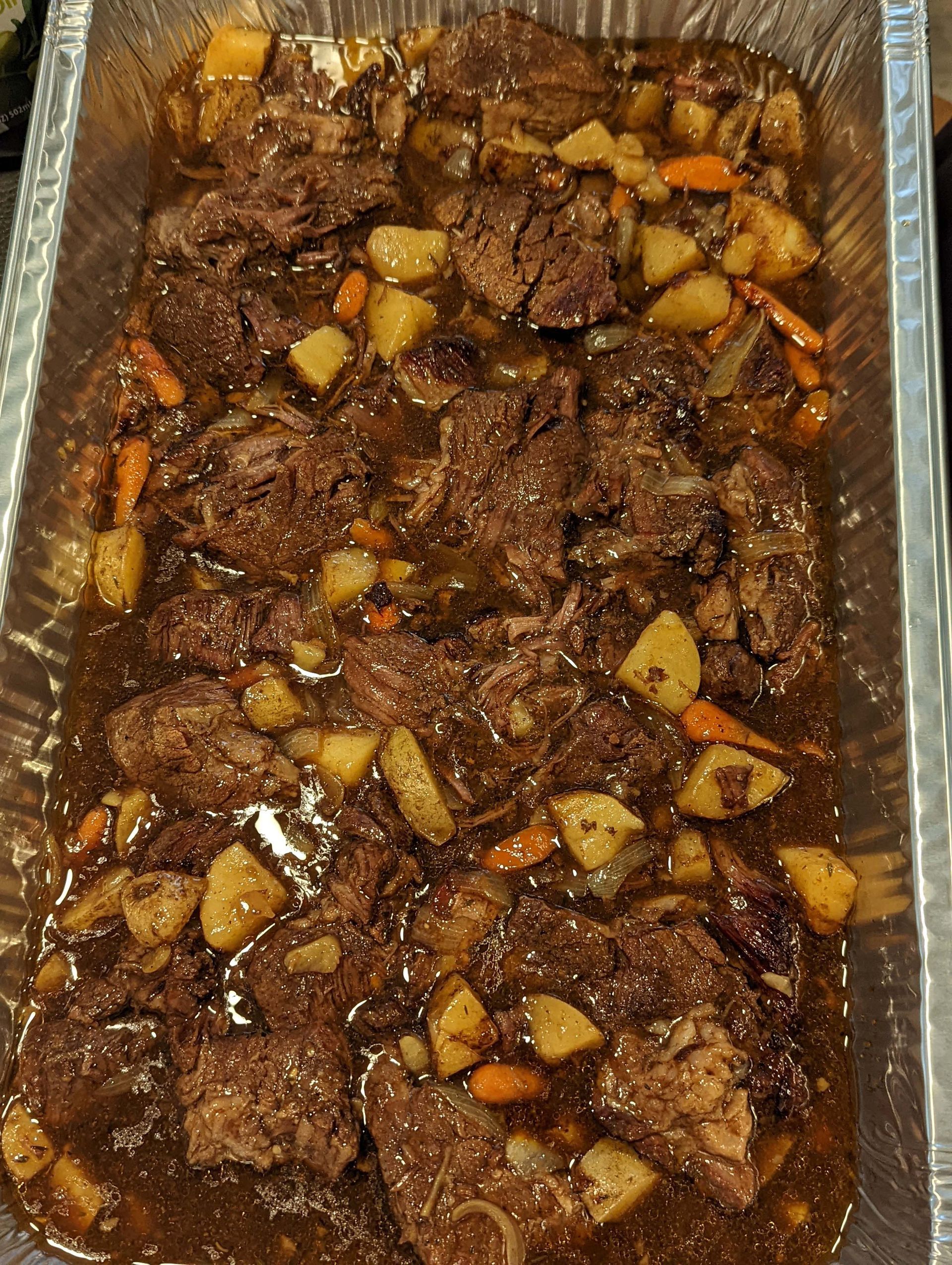 A casserole dish filled with meat , potatoes , carrots and gravy.