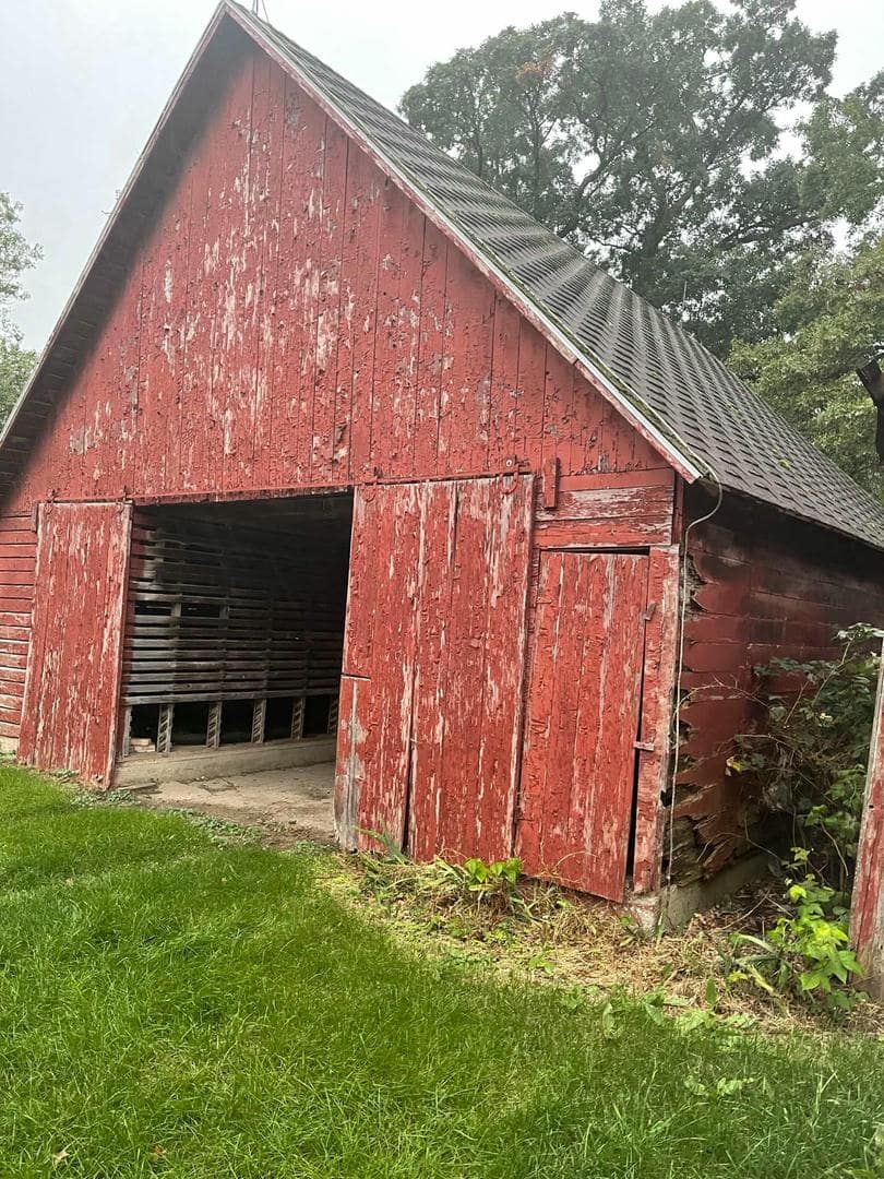 An old red barn is sitting in the middle of a grassy field.