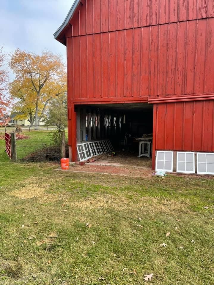 A red barn with the door open is sitting in the middle of a grassy field.