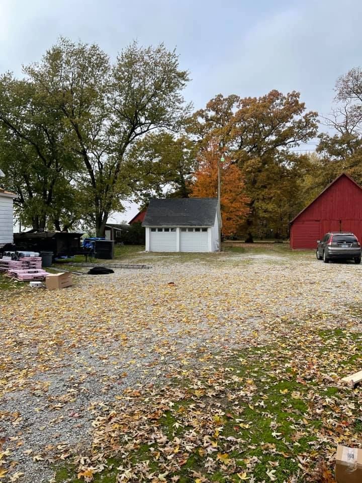 A car is parked in front of a garage next to a red barn.