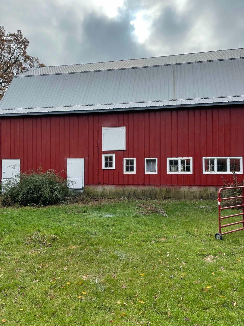 A red barn is sitting in the middle of a grassy field.