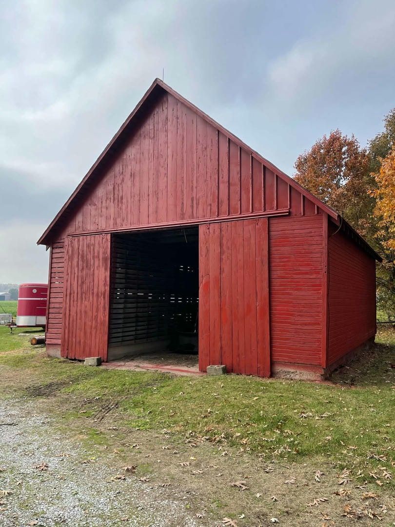 A red barn with its doors open is sitting in the middle of a grassy field.