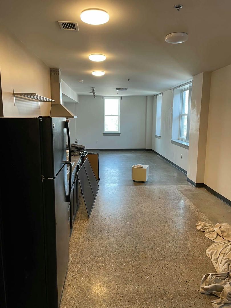 A large empty room with a black refrigerator and a stove.