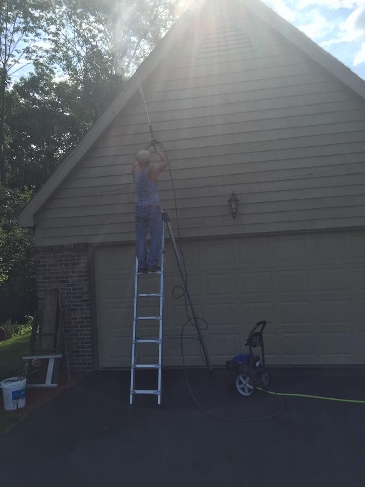 A Man Is Standing On A Ladder Cleaning The Side Of A House