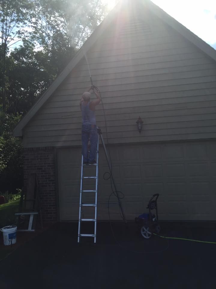 A Man On A Ladder Cleaning The Side Of A House