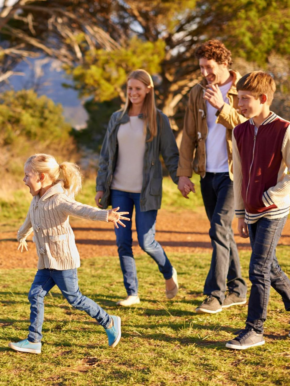 Family walking together in a sunny park, with a child running ahead on the grass.