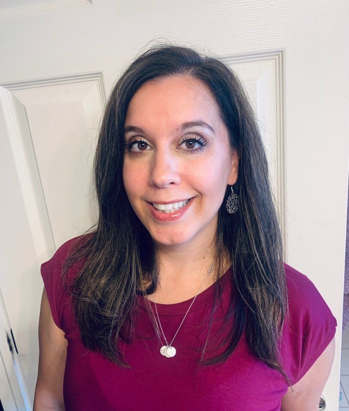 A woman wearing a purple shirt and a necklace is smiling for the camera.