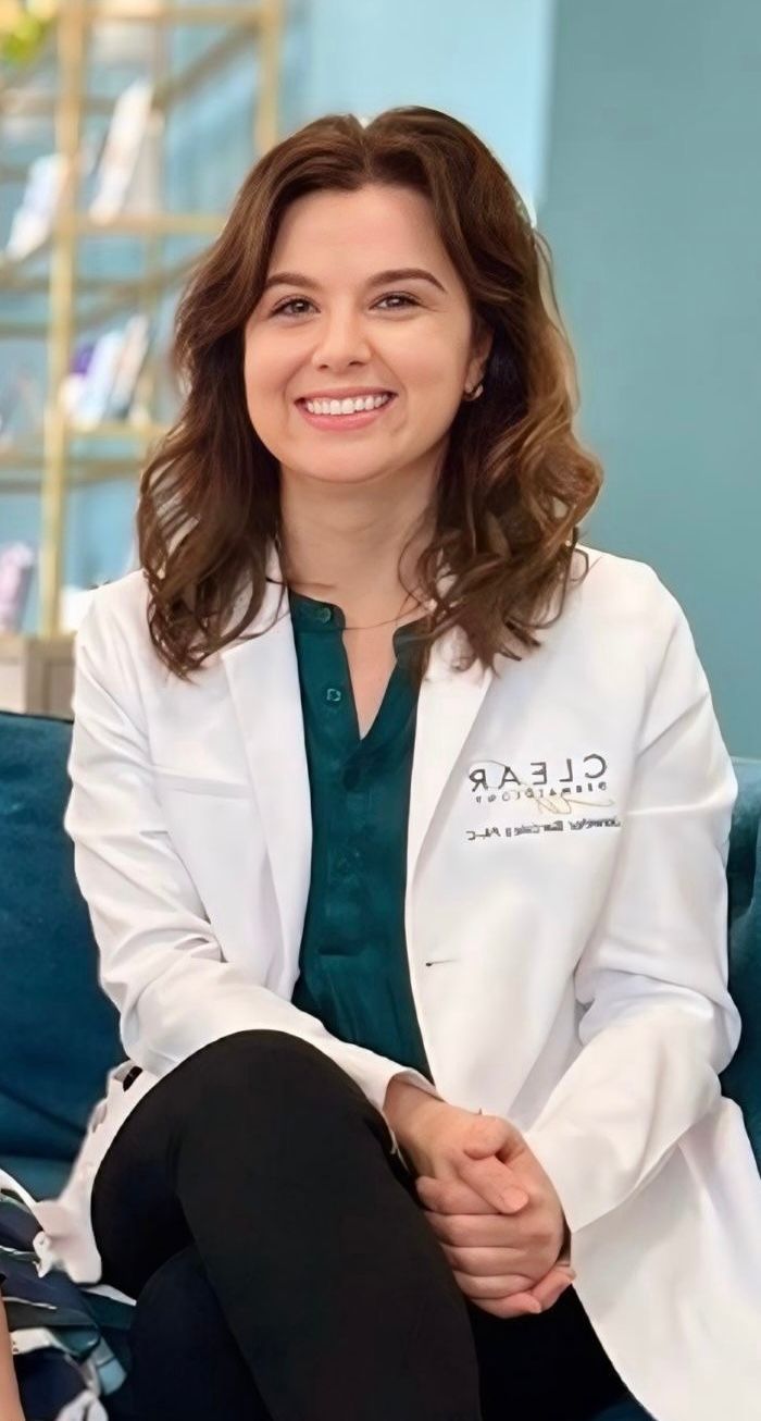 A woman wearing a purple shirt and a necklace is smiling for the camera.