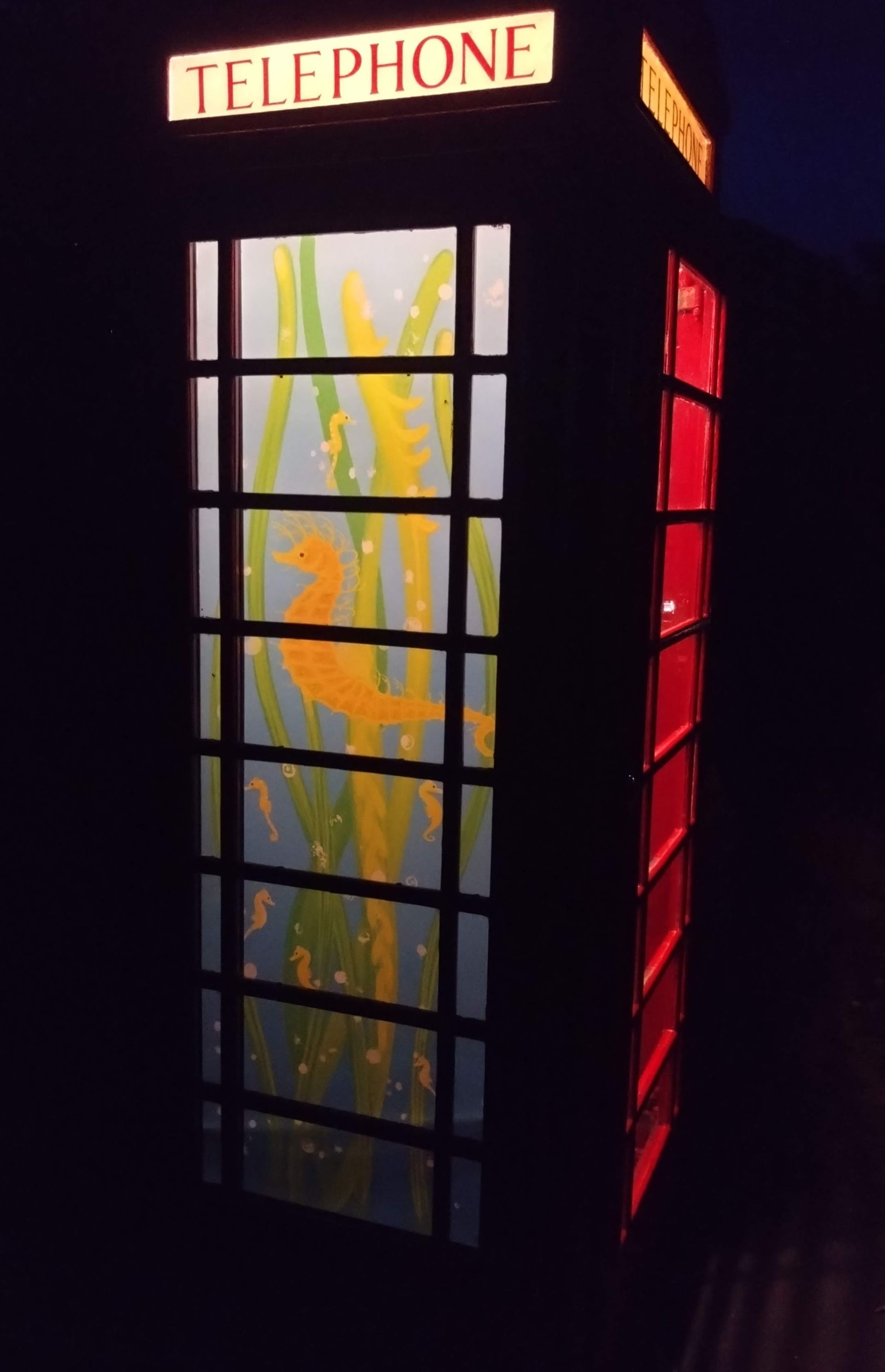 Illuminated vintage telephone booth with red sides and frosted glass panels at night