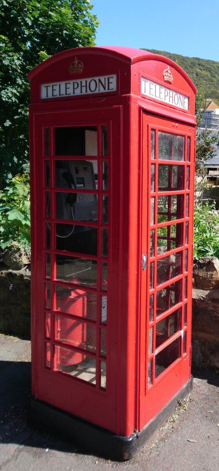 Red British phone booth with red door and window panels outdoors in sunlight