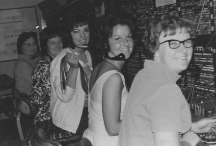 People standing at a counter in a dim indoor setting, one smiling toward the camera.
